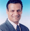 A smiling man in a formal suit against a blue background.