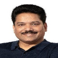 Person with a mustache smiling, wearing a navy shirt, against a white background.
