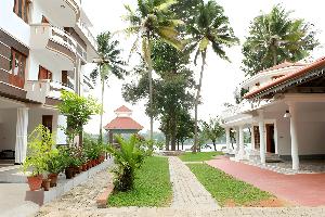 A scenic view of a tropical resort with palm trees, garden pathway, and two buildings near a water body.