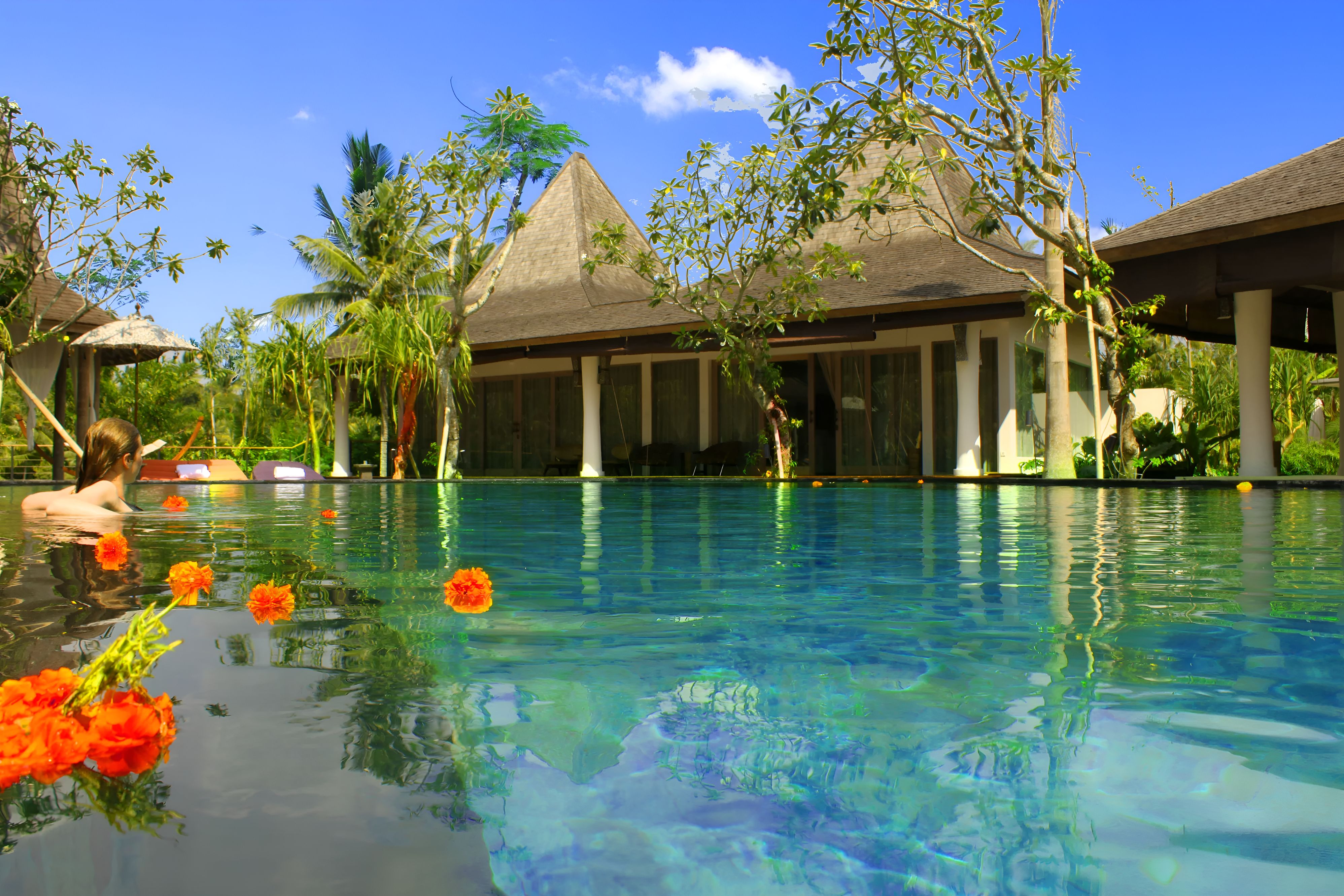 A serene pool surrounded by tropical greenery and buildings with thatched roofs under a clear blue sky.