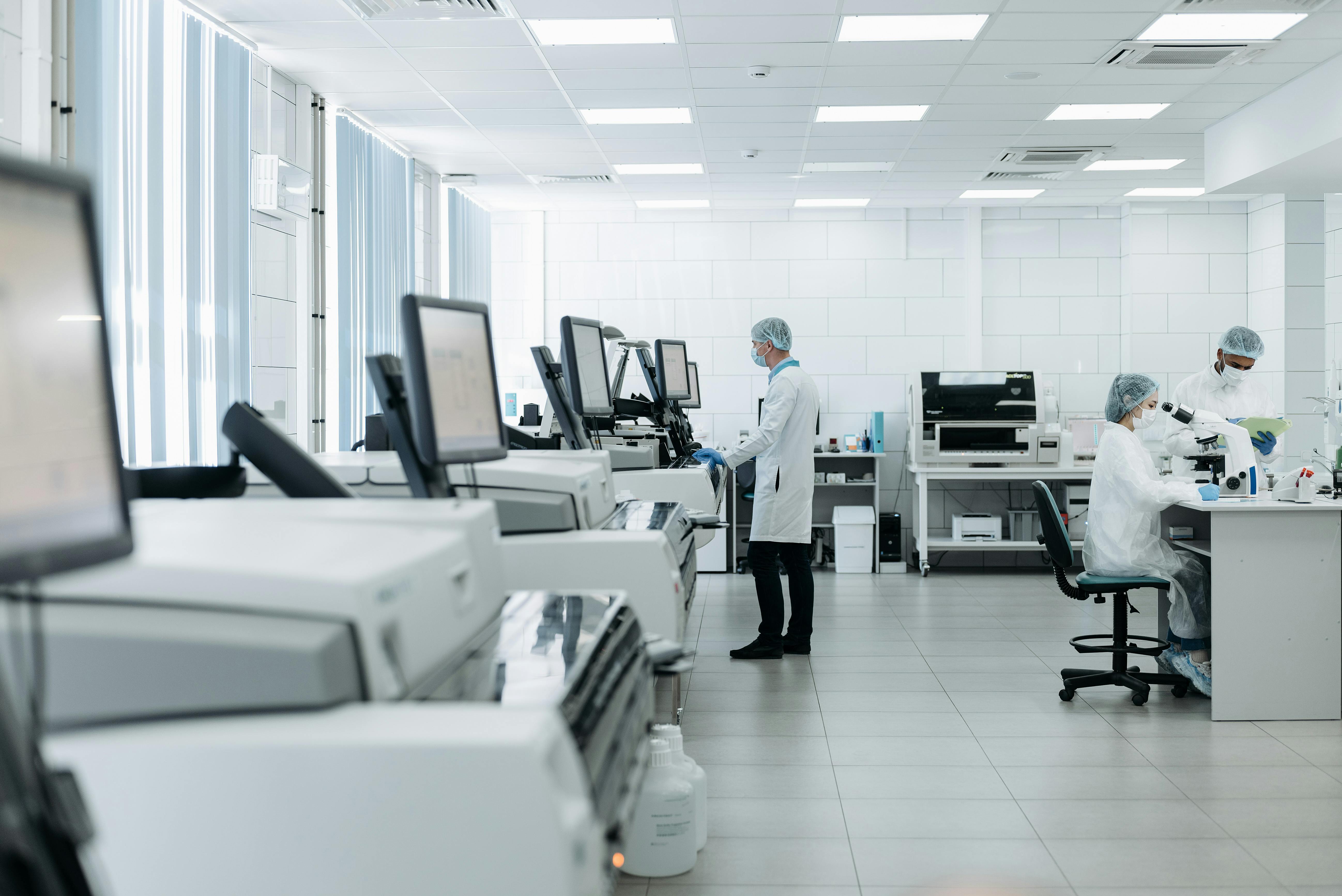 A modern laboratory with two workers in lab coats and medical masks, using equipment and computers.